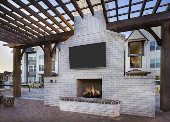 A fireplace with a TV above it is under a wooden pergola at Folksong Apartments, Flowery Branch, Georgia