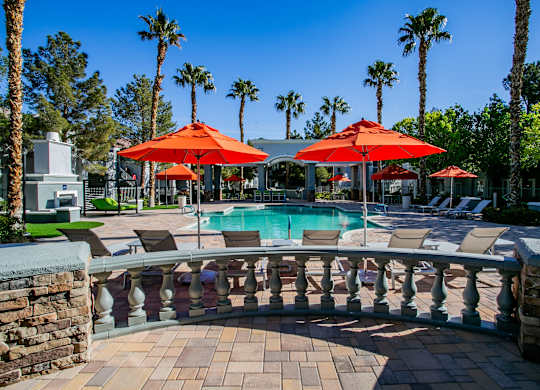 A pool area with red umbrellas and a stone wall.