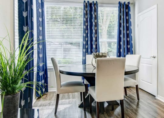 Separate dining area with large windows, window coverings, and a circular wooden table with four cream chairs at Tuscany Bay Apartments, Florida