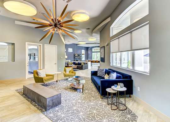 Community lounge area with a blue velvet sofa, modern pendant lighting, and windows at Tuscany Bay Apartments, Tampa, FL, 33626