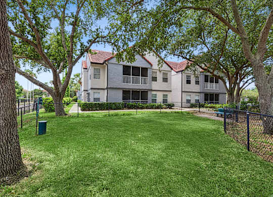 A large grassy area in front of a building with a fence and trees.