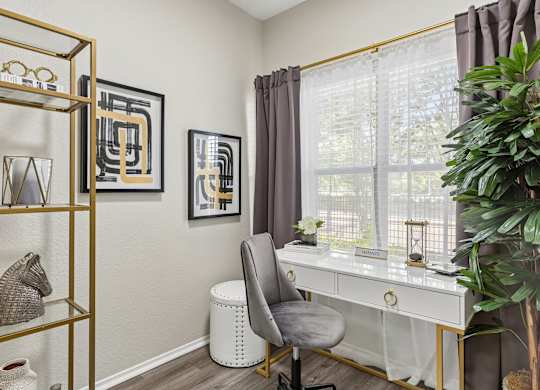 A room with a white desk, a grey chair, and a gold shelf with various objects on it.