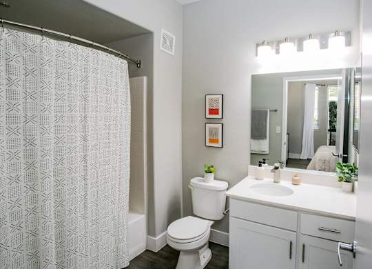 A white bathroom with a toilet, sink, and shower curtain. at Octave Apartments, Nevada