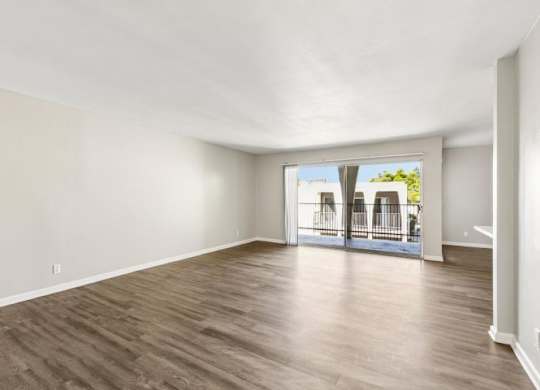 A room with wooden flooring and a sliding glass door leading to a balcony.