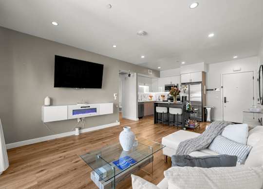 A modern living room with a white sofa, a glass coffee table, and a flat-screen TV mounted on the wall.