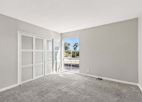 A room with a carpeted floor and a view of the outside through a glass door.