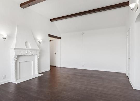 A room with a white fireplace and wooden beams on the ceiling.