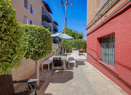 A patio with a table and chairs is surrounded by a brick wall and a green bush.