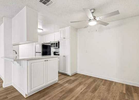 A white kitchen with a wood floor and a ceiling fan.
