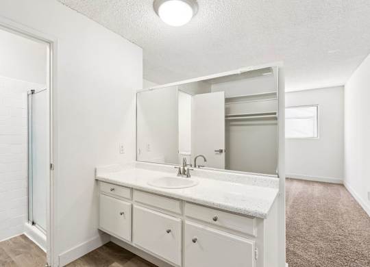 A white bathroom with a sink, mirror, and cabinets.