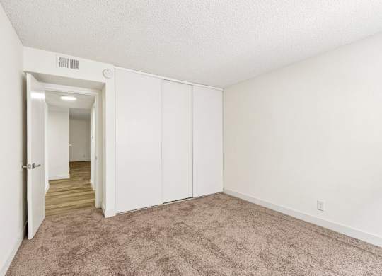 A room with white walls and carpeted floor with a doorway leading to another room.
