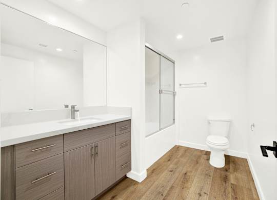 A white toilet sits in a bathroom with a white sink and wooden floors.