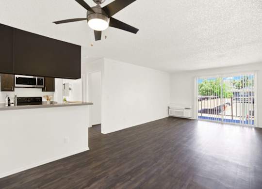 A room with a ceiling fan and a kitchen area with white cabinets at Monterra Ridge Apartments, Canyon Country