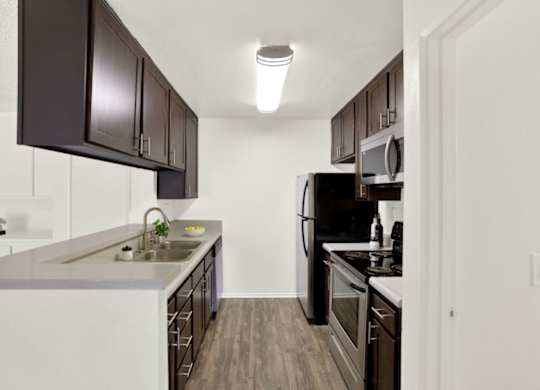 A kitchen with dark brown cabinets and white appliances at Monterra Ridge Apartments, Canyon Country