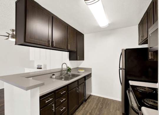A kitchen with dark brown cabinets and a black refrigerator at Monterra Ridge Apartments, Canyon Country