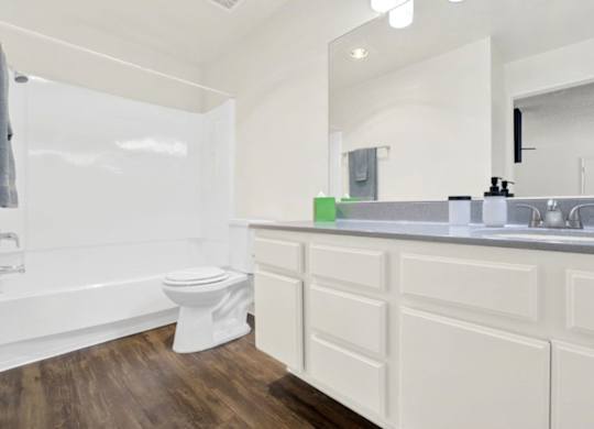 A white bathroom with a toilet, sink, and mirror at Monterra Ridge Apartments, Canyon Country