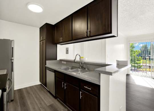 A kitchen with dark wood cabinets and a white sink at Monterra Ridge Apartments, Canyon Country