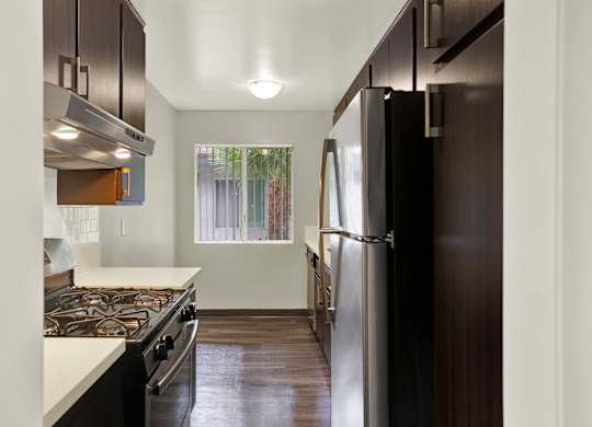 A modern kitchen with dark wood floors and stainless steel appliances at The Square in Downey, CA, 90242