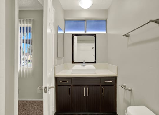 A bathroom with a sink, mirror, and toilet at The Square in Downey, CA, 90242
