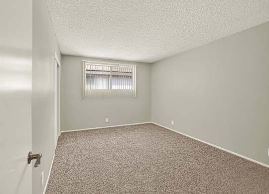 A room with a carpeted floor and a window with blinds at The Square in Downey, CA, 90242