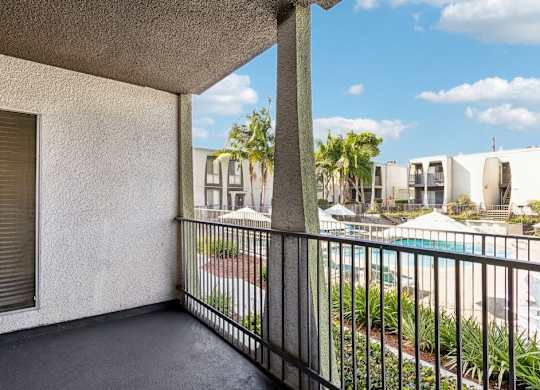A balcony with a black railing and a view of a pool and other buildings.