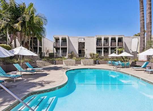 A swimming pool surrounded by lounge chairs and umbrellas with a building in the background.