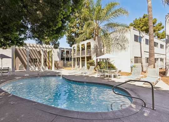 A swimming pool surrounded by lounge chairs and umbrellas in a residential area.