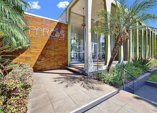 Property entrance sign with landscaping and palm trees at Parc @ 5 Apartments, Downey, CA 90240