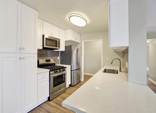 White galley kitchen with peninsula and stainless steel appliances at Parc @ 5 Apartments, Downey, 90240