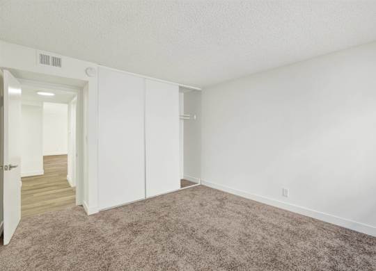 Carpeted bedroom with sliding closet doors at Parc @ 5 Apartments, Downey, CA