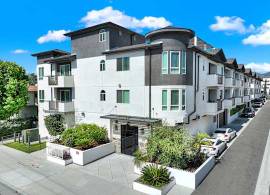 A row of modern townhouses with white and grey exteriors and green plants in front.