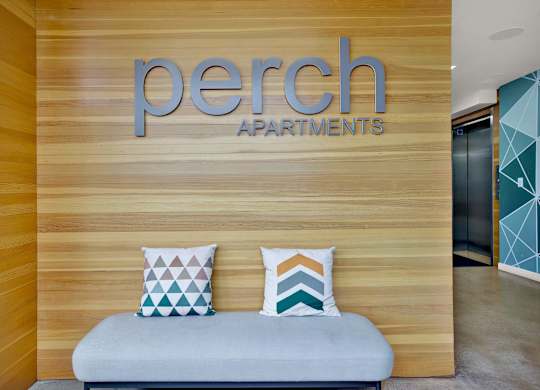 a bench with pillows in front of a building with a sign on the wall at the perch, California, 90065