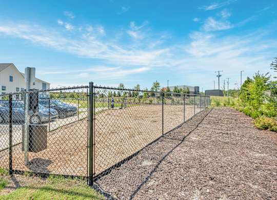 A chain link fence separates a gravel area from a grassy area.