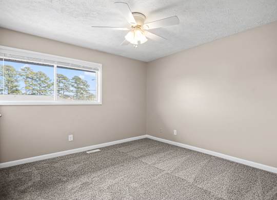 A room with a ceiling fan and a window showing trees outside.
