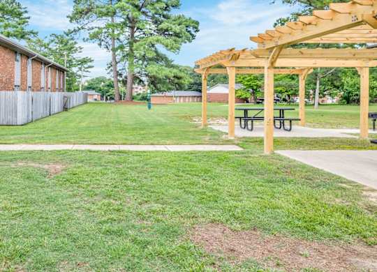 A grassy area with a wooden pergola and picnic tables.