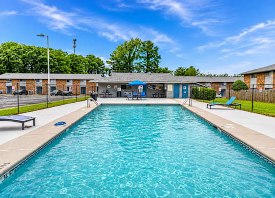 A large outdoor swimming pool with a blue sky and trees in the background.
