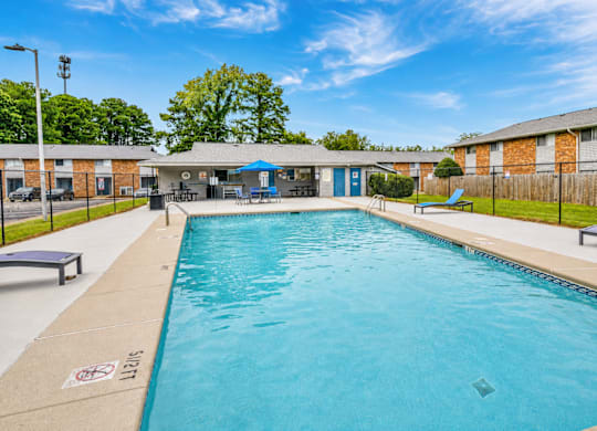 A large outdoor swimming pool with a blue sky and trees in the background.