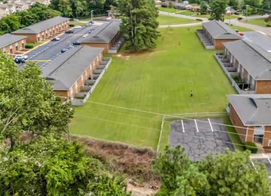 A parking lot is in front of a building with a green lawn in the middle.