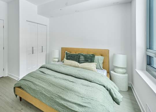 a bedroom with white walls and a bed with grey blankets and pillows