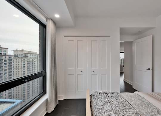 A bedroom with a large bed and a view of a cityscape through a window.