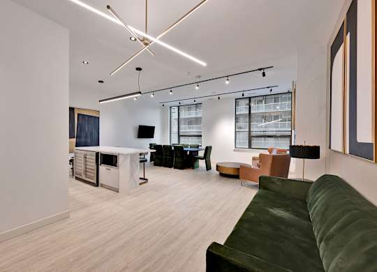 A modern living room with a green couch and a kitchen area in the background.