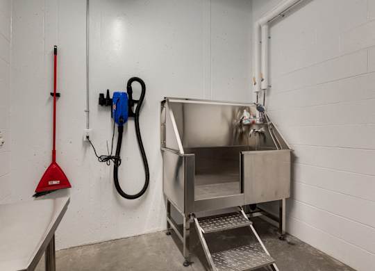 A red plunger is leaning against a white wall next to a blue and black vacuum cleaner.