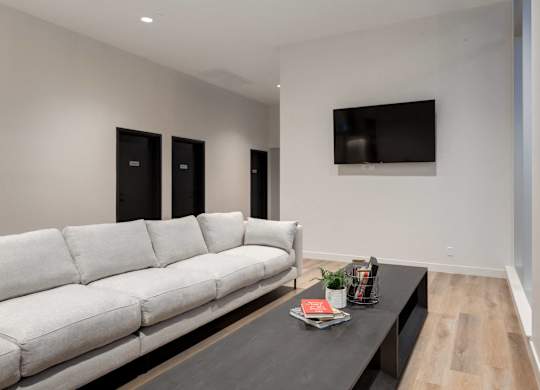 A white couch sits in a room with a black coffee table and a flat screen TV mounted on the wall.