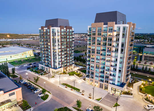 Two modern high-rise buildings are surrounded by a parking lot and other buildings.