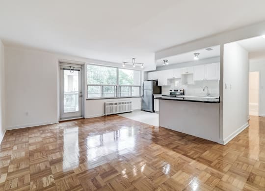 an empty living room with a kitchen and a large window