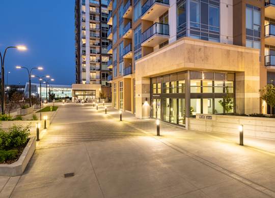 A long concrete walkway leads to a building with glass windows and doors.