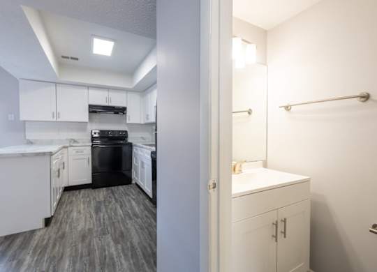 A white kitchen with a black dishwasher and a white bathroom with a white sink.