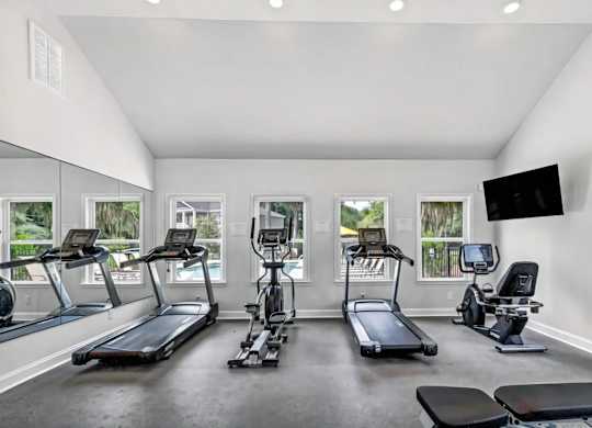 A spacious home gym with treadmills, elliptical machines, and a television.