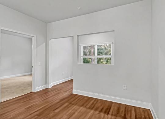 A room with white walls and wooden flooring with a window.