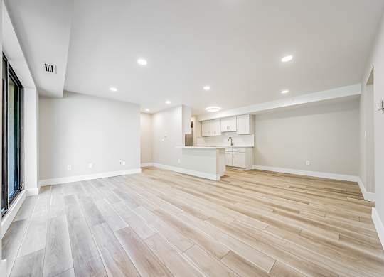A spacious room with wooden flooring and a kitchenette in the background.